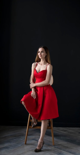Porträt einer jungen Frau in einem roten Kleid, die auf einem hohen Barhocker sitzt