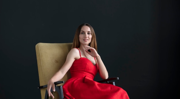 Porträt einer jungen Frau in einem roten Kleid, die auf einem Stuhl sitzt