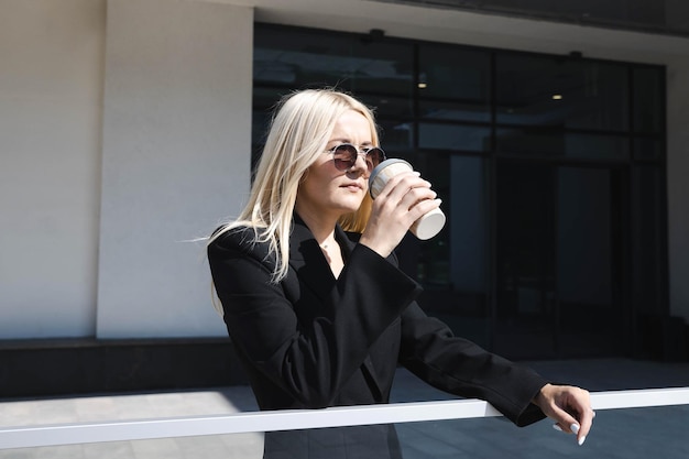 Porträt einer jungen Frau in einem stilvollen Anzug, die auf der Straße Kaffee trinkt