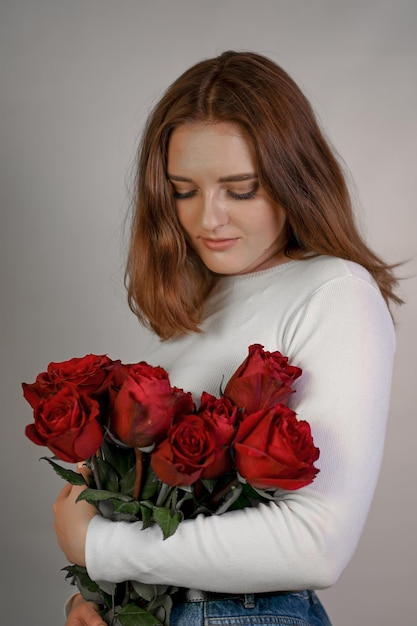 Porträt einer jungen Frau in einer weißen Bluse mit einem Rosenstrauß auf einem rosa Hintergrund Valentinstag