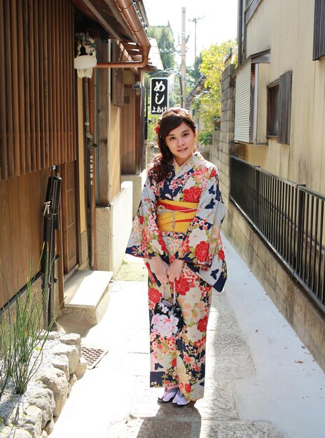 Foto porträt einer jungen frau in kimono, die in einer gasse zwischen den häusern steht