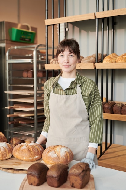 Porträt einer jungen Frau in Schürze, die in die Kamera schaut, während sie in der Bäckerei steht