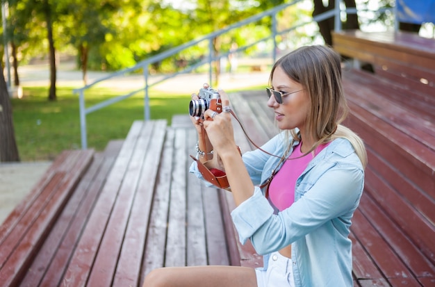 Porträt einer jungen Frau in stilvoller Kleidung, die eine Retro-Kamera im Freien hält