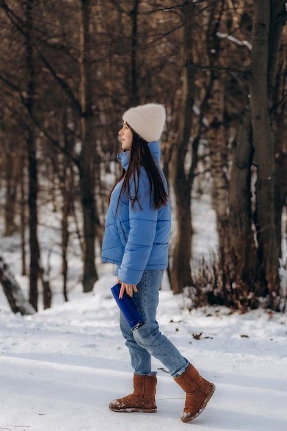 Porträt einer jungen Frau in warmer Kleidung im Winterwald, die draußen heißen Tee aus einer Thermoskanne trinkt und beim Wandern hochwertiges Foto macht