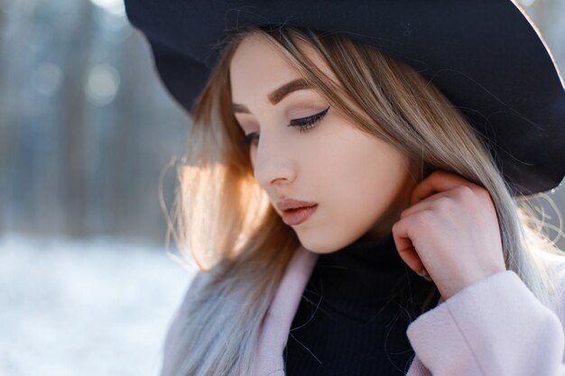 Porträt einer jungen Frau mit braunen Augen mit sexy Lippen mit blondem Haar mit schönem Make-up in einem eleganten schwarzen Hut