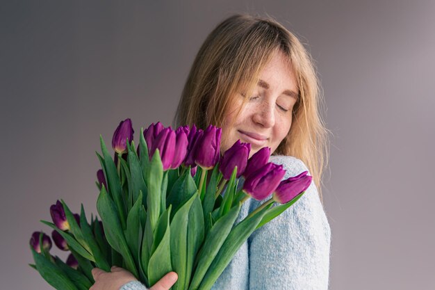 Porträt einer jungen Frau mit einem Strauß Tulpen auf grauem Hintergrund