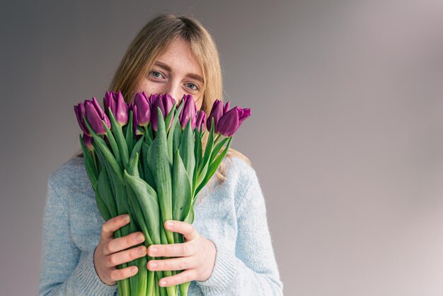 Porträt einer jungen Frau mit einem Strauß Tulpen auf grauem Hintergrund