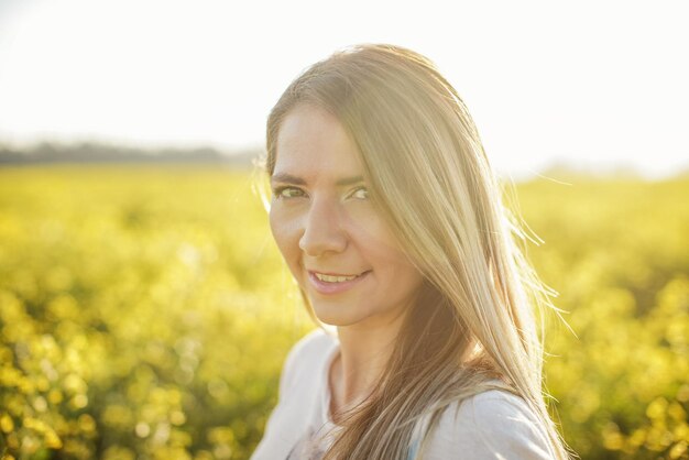 Porträt einer jungen Frau mit langen Haaren, gelbem Blumenfeld und Sonnenhintergrundbeleuchtung hinter ihr