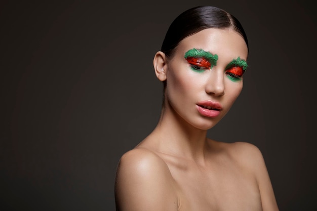 Porträt einer jungen Frau mit leuchtend rotem und grünem kreativem Make-up auf dunklem Hintergrund Schönheitsmode