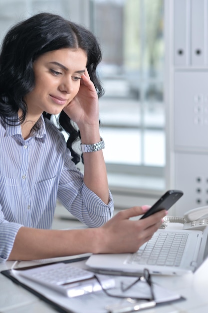 Porträt einer jungen Frau mit Smartphone und Laptop