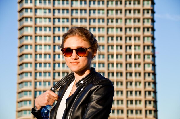 Porträt einer jungen Frau mit Sonnenbrille, die an einem Gebäude in der Stadt steht
