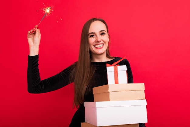 Porträt einer jungen Frau mit Weihnachtsgeschenken und Wunderkerzen auf rotem Grund