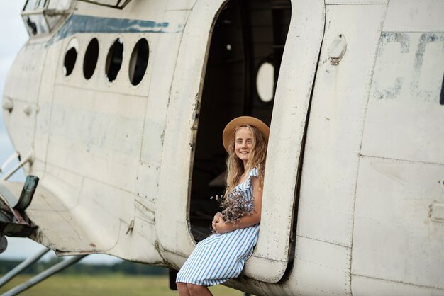 Porträt einer jungen Frau nahe einem Retro-Flugzeug. in Hut und Blumen