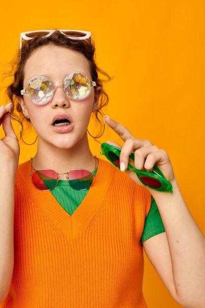 Porträt einer jungen Frau, orangefarbene Sweatshirts, Sonnenbrillen, bunte Gläser, liefern unveränderten Lebensstil