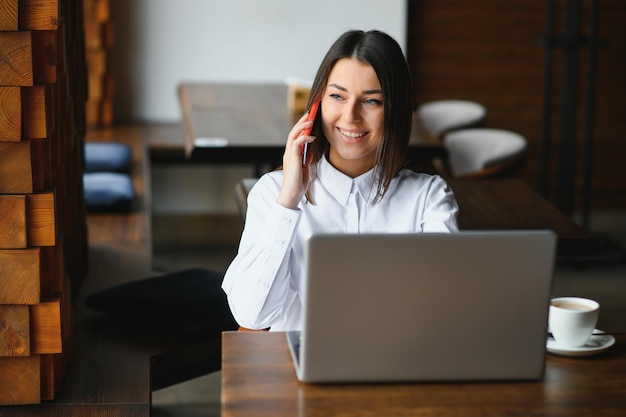 Porträt einer jungen Freiberuflerin, die Laptop-Computer für Fernjobs verwendet, während sie im modernen Café-Interieur sitzt, intelligente blonde Frau, die beim morgendlichen Frühstück in der Café-Bar am Net-Book arbeitet