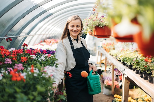 Porträt einer jungen Gärtnerin, die Blumen in einem Gewächshaus bewässert und täglich Pflanzen pflegt