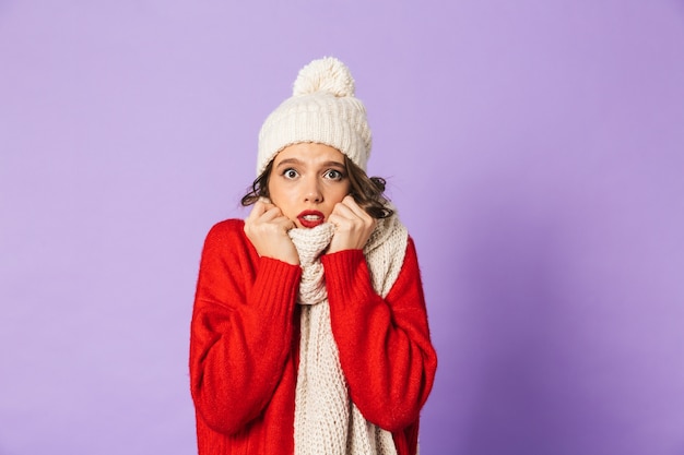 Porträt einer jungen gefrorenen Frau, die Wintermütze und Schal trägt, lokalisiert über lila Wand.