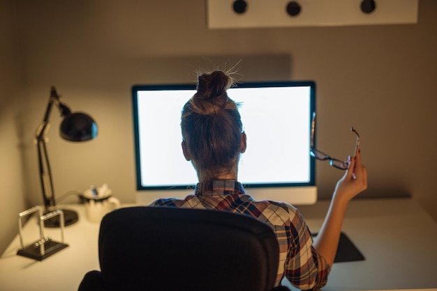 Porträt einer jungen Geschäftsfrau, die ihre Arbeit am Computer beendet und zu Hause eine Brille hält.