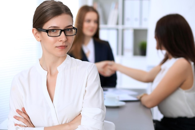 Porträt einer jungen Geschäftsfrau gegen eine Gruppe von Geschäftsleuten bei einem Treffen.