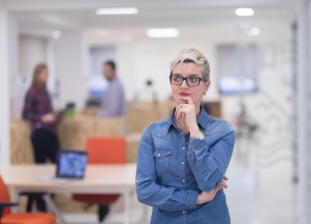 Porträt einer jungen Geschäftsfrau im modernen Startup-Büroinnenraum, Team bei der Besprechung im Hintergrund