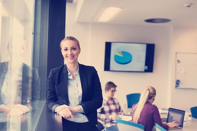 Porträt einer jungen Geschäftsfrau im modernen Startup-Büroinnenraum, Team in der Besprechungsgruppe im Hintergrund