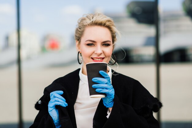 Porträt einer jungen Geschäftsfrau mit Telefon, Notizbuch, Tablette, Kaffee im Freien. Blondes Mädchen in blauen Gummihandschuhen.