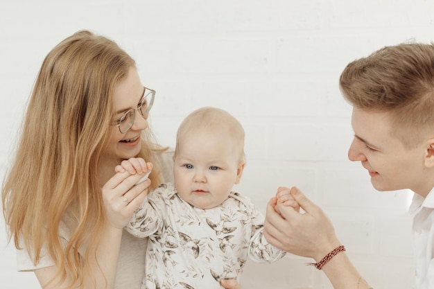 Porträt einer jungen, glücklich lächelnden, schönen Familie mit engelblauem, blauäugigem Säuglingskleinkind in Weiß