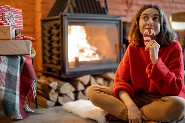 Porträt einer jungen glücklichen Frau mit einer Weihnachtssüßigkeit am Kamin während der Winterferien