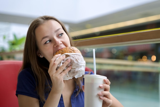 Foto porträt einer jungen glücklichen frau oder eines schönen teenagermädchens, das schnelles junkfood, leckeren burger und