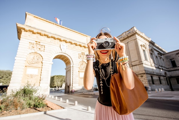 Porträt einer jungen glücklichen Touristin mit Fotokamera vor dem berühmten Triumphbogen während des Morgenlichts in der Stadt Montpellier, Frankreich