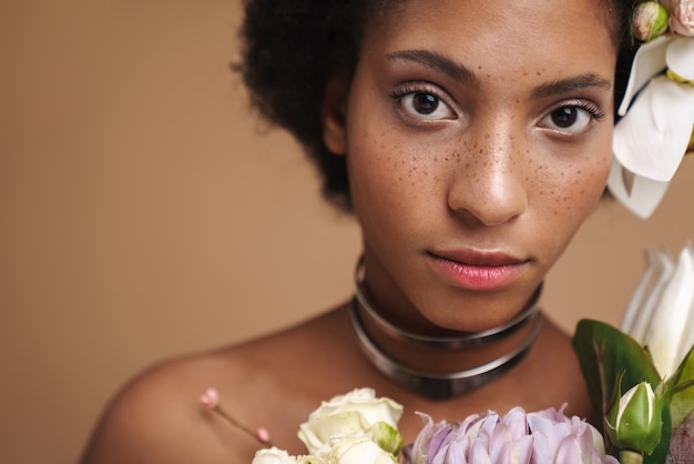 Porträt einer jungen halbnackten sommersprossigen Afroamerikanerin, die mit Blumen posiert