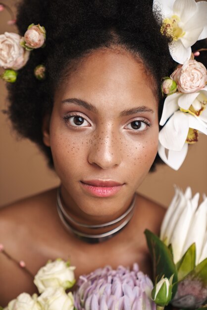 Porträt einer jungen halbnackten sommersprossigen Afroamerikanerin, die mit Blumen posiert