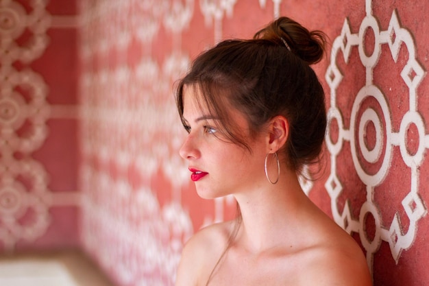 Porträt einer jungen hübschen Frau, die sich auf eine rosa gestaltete Wand mit weißem Ornament stützt