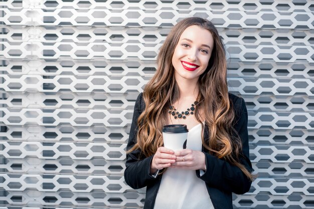Porträt einer jungen hübschen Geschäftsfrau mit Kaffee zum Mitnehmen auf dem Metallwandhintergrund