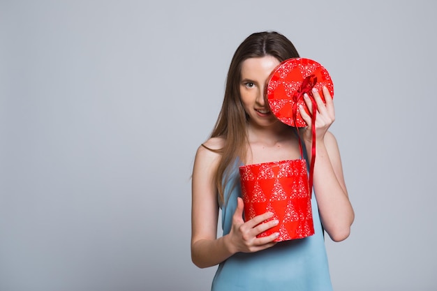 Porträt einer jungen, hübschen, süßen, glamourösen Mädchendame, die eine Geschenkbox mit grauem Oberteil trägt