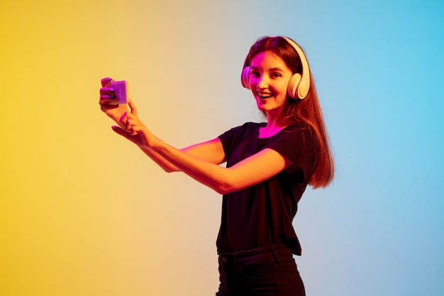 Porträt einer jungen kaukasischen Frau auf blau-gelbem Studiohintergrund mit Farbverlauf im Neonlicht