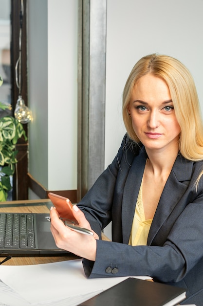 Porträt einer jungen kaukasischen Geschäftsfrau mit einem Smartphone und einem Laptop am Tisch