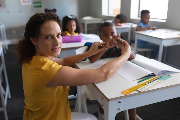 Porträt einer jungen kaukasischen Lehrerin, die einem afroamerikanischen Jungen beim Lernen der Gebärdensprache hilft