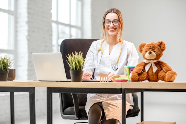 Porträt einer jungen Kinderärztin im medizinischen Kittel, die im Büro sitzt