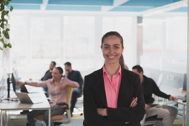 Porträt einer jungen lächelnden Geschäftsfrau in einem kreativen Open-Space-Coworking-Startup-Büro. Erfolgreiche Geschäftsfrau, die im Büro mit copyspace steht. Kollegen, die im Hintergrund arbeiten.