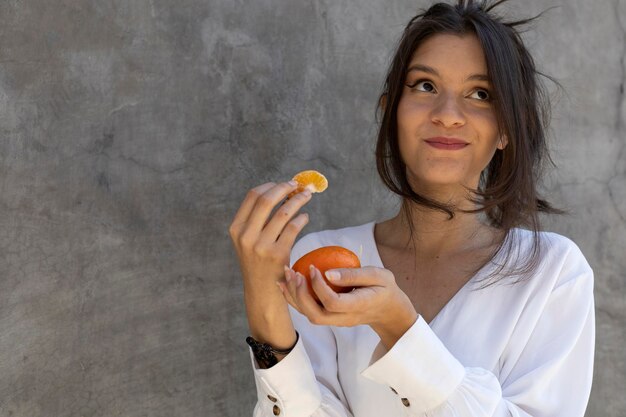 Porträt einer jungen lateinamerikanischen Frau 24, die eine leckere Mandarine isst Gesundes Ernährungskonzept