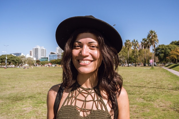Porträt einer jungen lateinamerikanischen Frau mit Hut und Lächeln an der Küste der Stadt, die in die Kamera schaut
