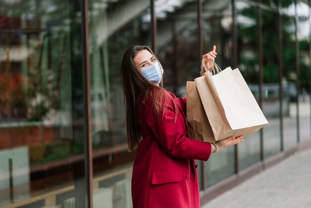 Porträt einer jungen Modefrau mit Schutzmaske mit Einkaufstüten auf der Stadtstraße