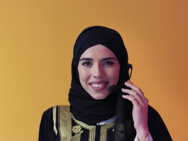 Porträt einer jungen muslimischen Frau mit Kopfhörern, die als Call-Center-Betreiberin isoliert auf gelbem Hintergrund arbeitet