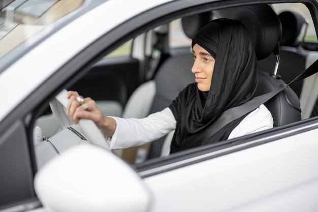 Porträt einer jungen muslimischen Geschäftsfrau mit einem Hijab auf dem Kopf, der ein Auto fährt. Konzept der Globalisierung und Modernisierung der islamischen Gesellschaft und Frauenrechte