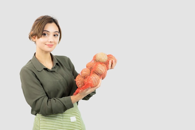 Porträt einer jungen reizenden Landwirtfrau, die Kartoffeln in der Tasche hält. Foto in hoher Qualität