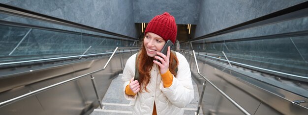 Foto porträt einer jungen rothaarigen frau, die durch die stadt geht und mit eingeschaltetem mobiltelefon die treppe hinaufsteigt