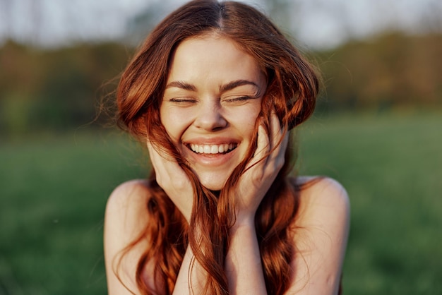 Porträt einer jungen rothaarigen Frau, die in die Kamera blickt und lächelt. Nahaufnahme einer lachenden Frau im untergehenden Sonnenlicht