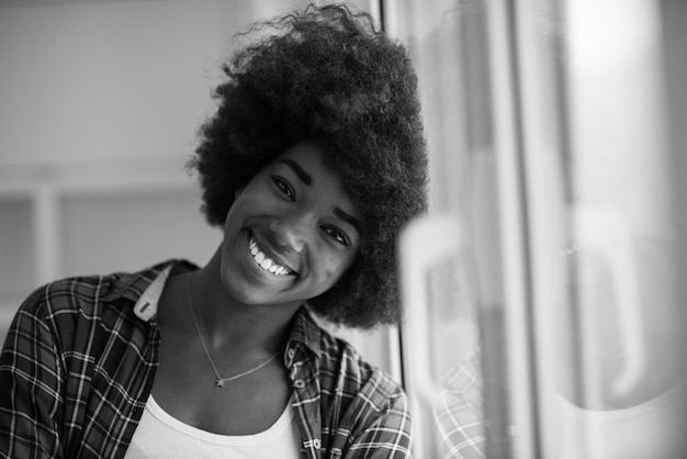 Porträt einer jungen schönen afroamerikanischen Frau mit lockigem Haar in der Nähe des Fensters