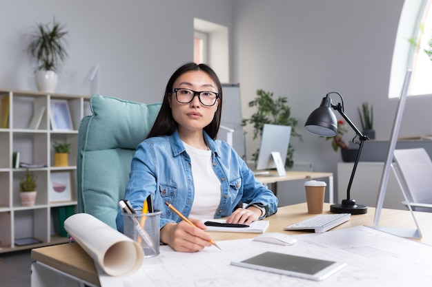 Porträt einer jungen schönen asiatischen Architektin mit Brille, die an einem Schreibtisch an einem Computer arbeitet und